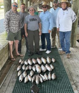 A group of men standing before their catch, which is laid out on the pier deck.