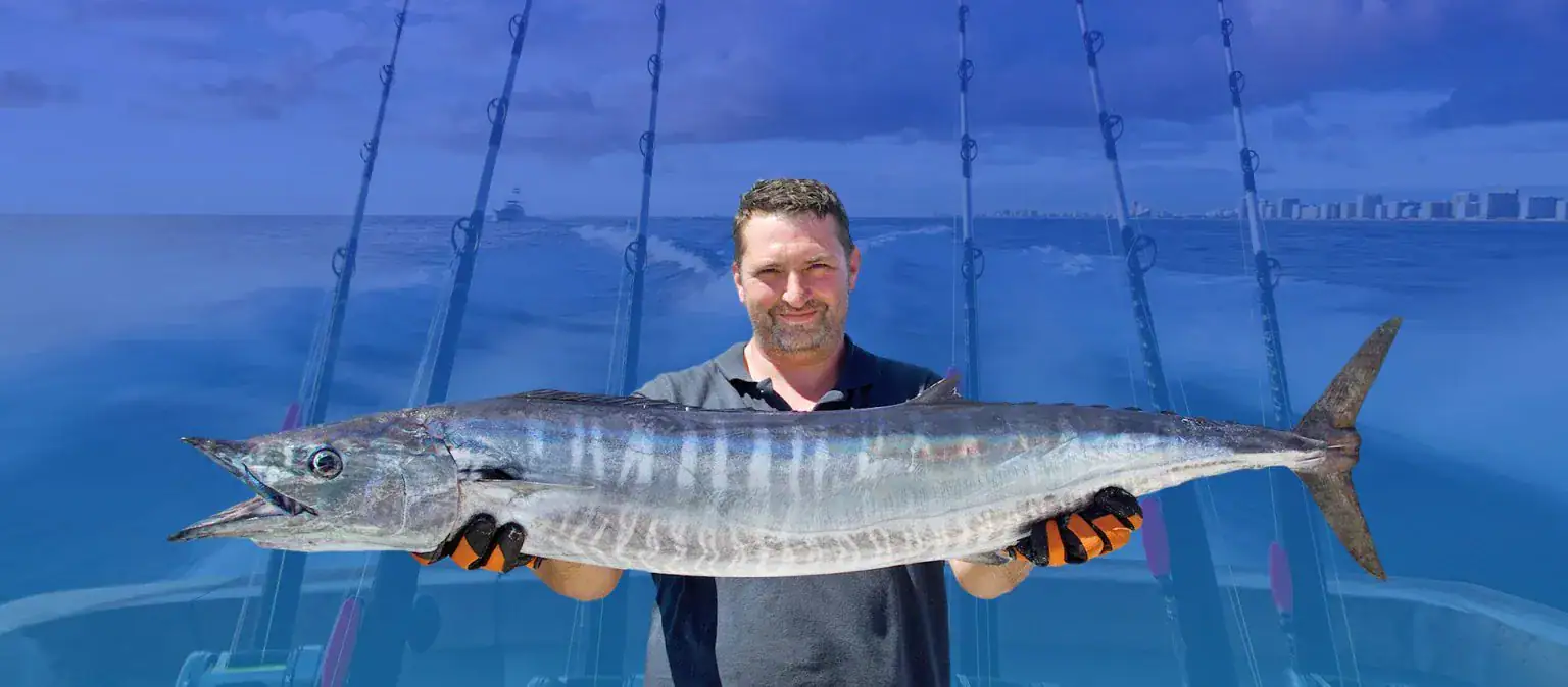 Guy standing in the back of a boat holding up a big fish.